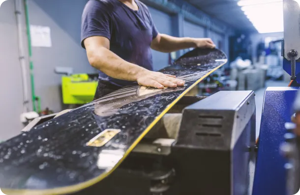 about_crystal_systems Technician working on snowboard using industrial equipment, representing precision manufacturing in sporting goods production.