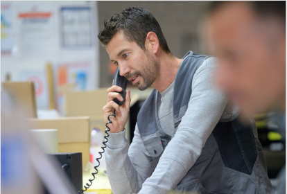 sales-representative-talking-on-phone-in-warehouse Sales representative in warehouse environment talking on phone while managing orders and inventory from computer workstation.